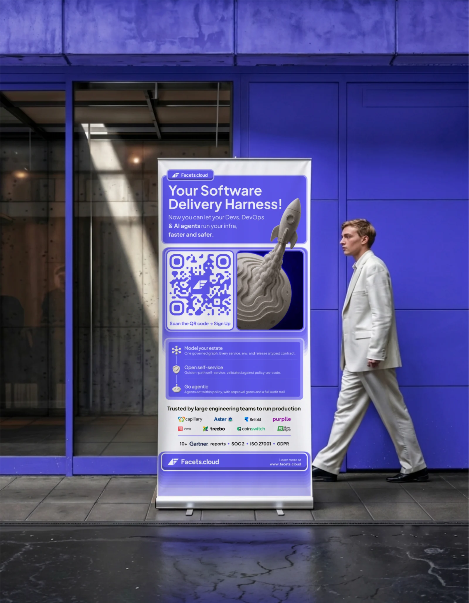 mockup of a facets.cloud roll-up banner on a wet pavement outside a purple building. the banner reads 'your software delivery harness', with a qr code, a rocket illustration, three product points and a row of customer logos. a figure in a pale suit walks past it for scale.
